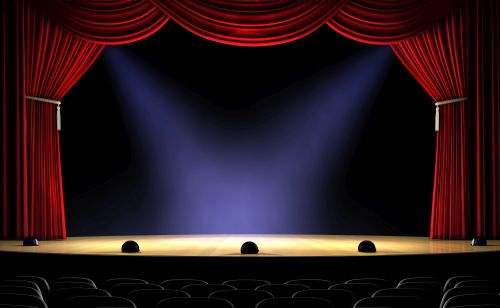 An empty theater stage with lights on center stage and the curtains up